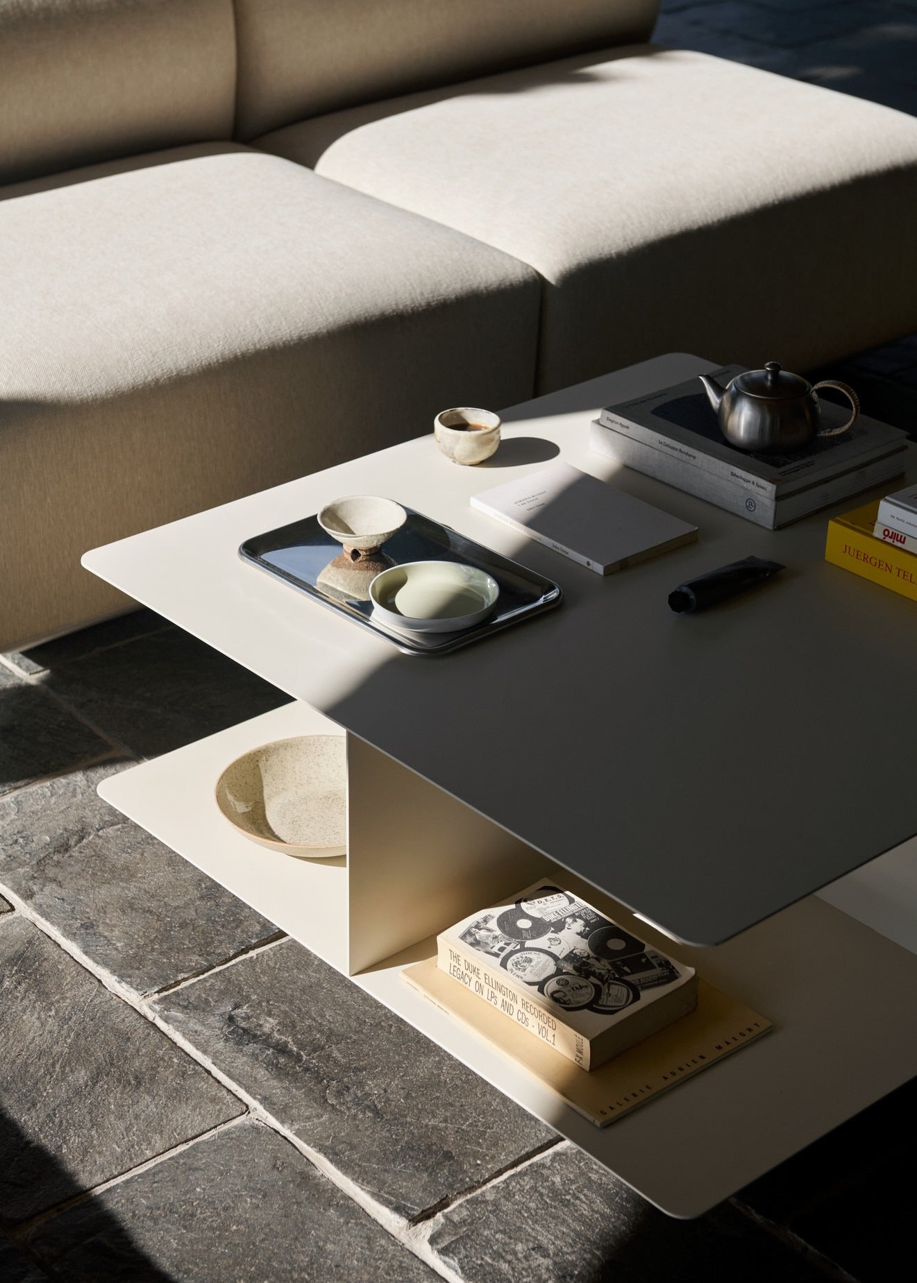 Mesa de centro Develius EV3 de &Tradition en acero lacado en polvo, diseño minimalista de Edward van Vliet sobre fondo neutro; Develius Coffee Table EV3 — 155881A576_Develius EV3_Stone Grey_Angled Front; Develius Coffee Table EV3 — ATD_Retail_2026_Develius EV3_Develius EV1C; Develius Coffee Table EV3 — 155881A410_Develius EV3_Ivory_Detail; Develius Coffee Table EV3 — ATD_Retail_2026_Develius EV3_Mist AP21_Momento Vase JH41_Mnemonic MNC4_02