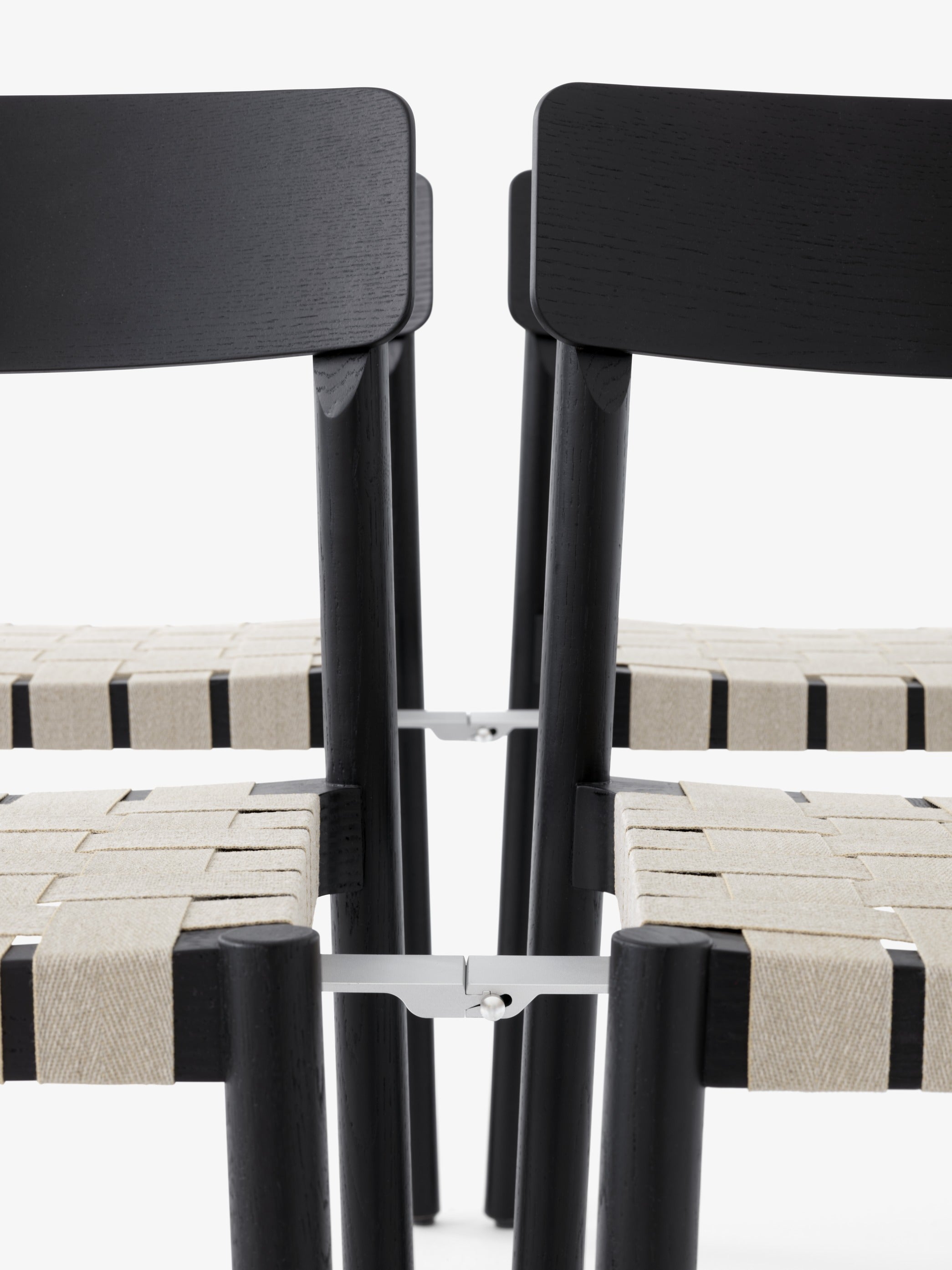 Silla de comedor Betty TK1 de &Tradition con estructura de madera maciza, respaldo de chapa y asiento con cinta de lino; Betty Side Chair TK1 — Betty TK1_Smoked oak w. natural webbing_angled front; Betty Side Chair TK1 — Betty TK1_Oak.front; Betty Side Chair TK1 — Betty TK1 Black w. linking system_rows_front; Betty Side Chair TK1 — ATD_Location_2019_Betty_TK1_InBetween_SK12