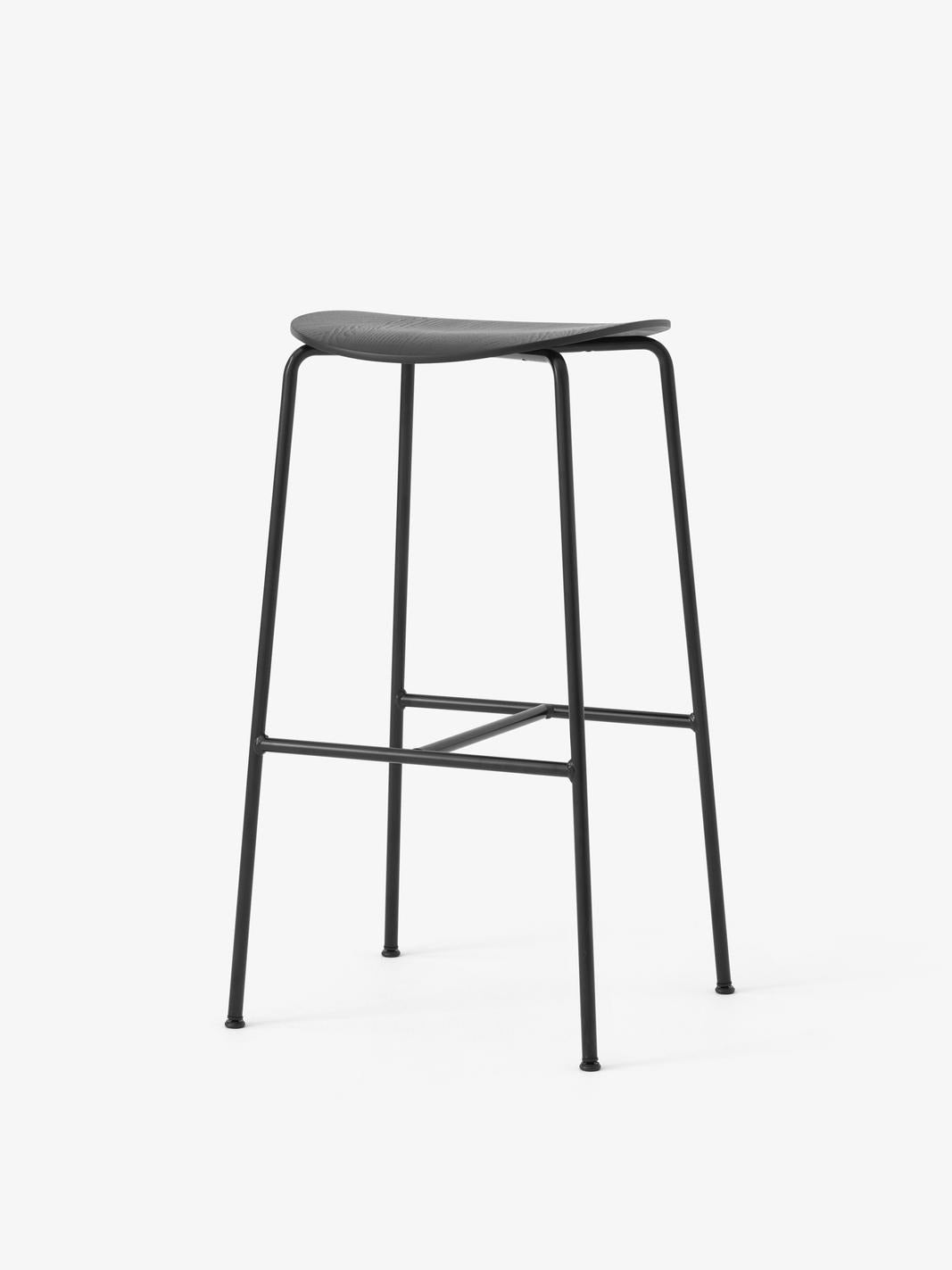Taburete de bar &Tradition Pavilion AV38 con estructura de tubos de acero y asiento de chapa moldeada diseñado por Anderssen ; Pavilion Bar Stool AV38 — Pavilion Bar Stool AV38_Black frame_Black Lacquered Oak_Angled Front; Pavilion Bar Stool AV38 — Pavilion Bar Stool AV38_Black frame_Lacquered Oak_Angled Front